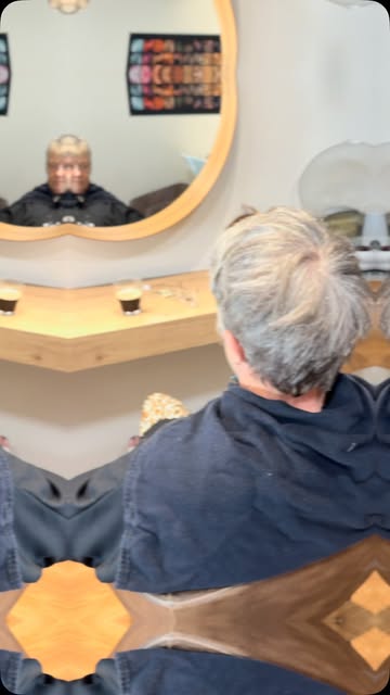 Une cliente coiffée devant le miroir rond du salon